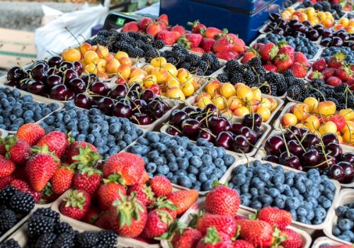 Colorful berries and stone fruits arranged in neat crates at a market, with ripe strawberries, blueberries, cherries, and apricots. Top it at 140 characters, always ending the sentence.