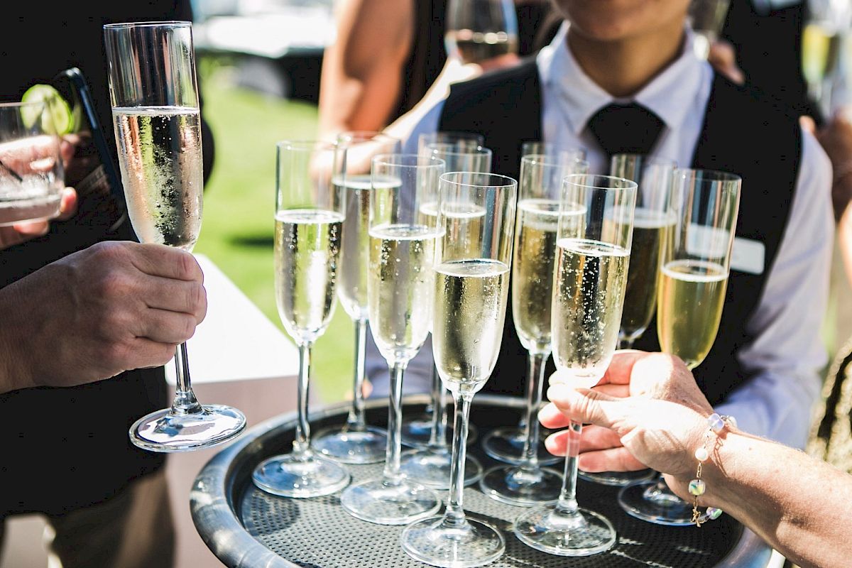A group of people toasting with tall champagne flutes on a tray at an outdoor event, celebrating a moment together.