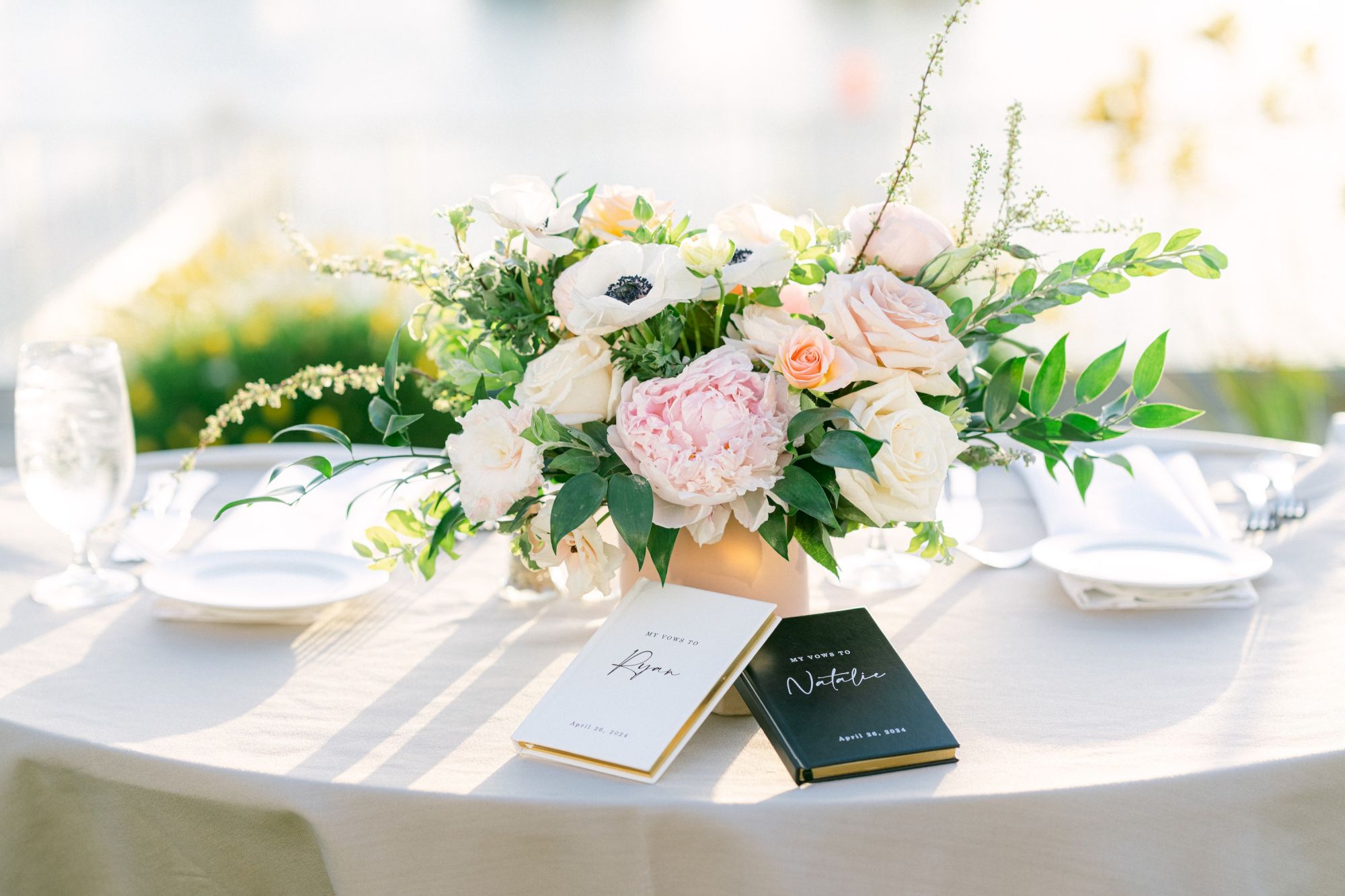 A wedding-style table setting with a lush floral centerpiece, menus, plates, and glassware arranged on a white-clothed table.