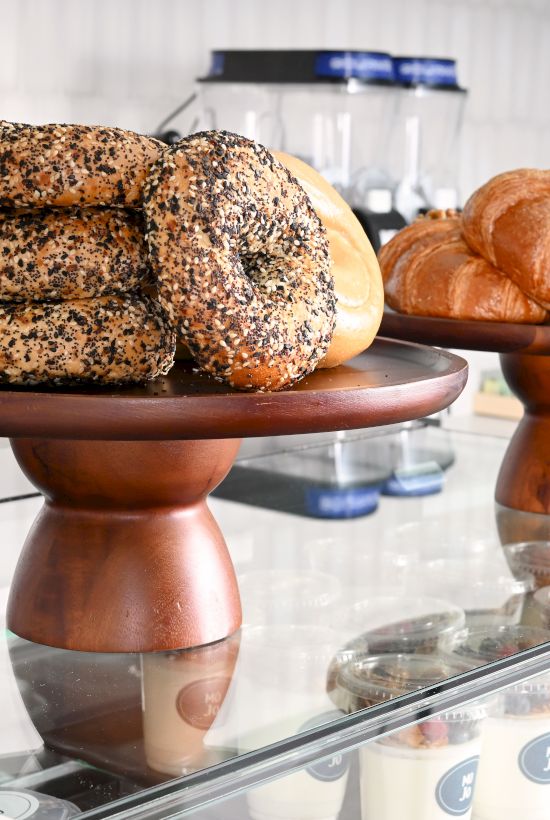 A pastry display with sesame-covered bagels and golden croissants on a stand, fresh in a bakery case.