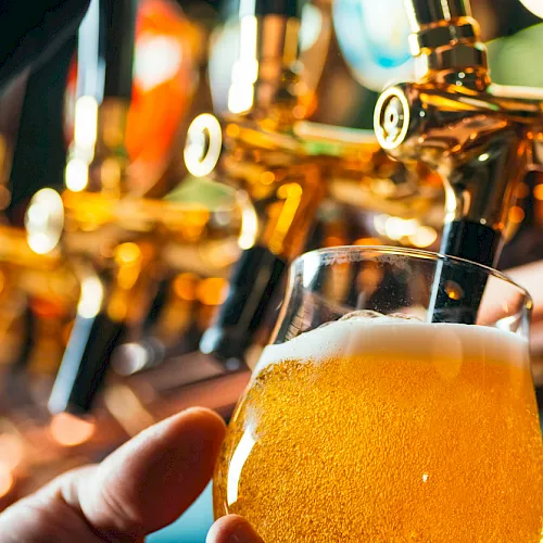A person holds a foamy pint of beer while it&rsquo;s poured from a shiny tap in a bar.