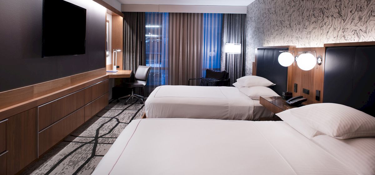 A modern hotel room with two white beds, dark wood paneling, and floor-to-ceiling curtains by a window.