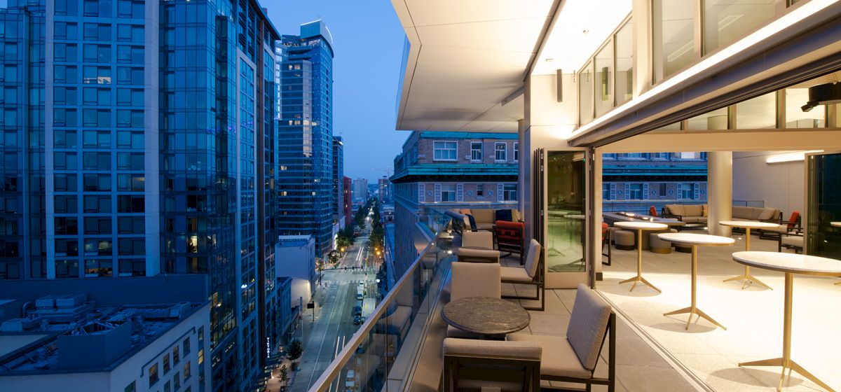 A modern rooftop terrace with lounge chairs overlooks downtown skyscrapers at dusk.
